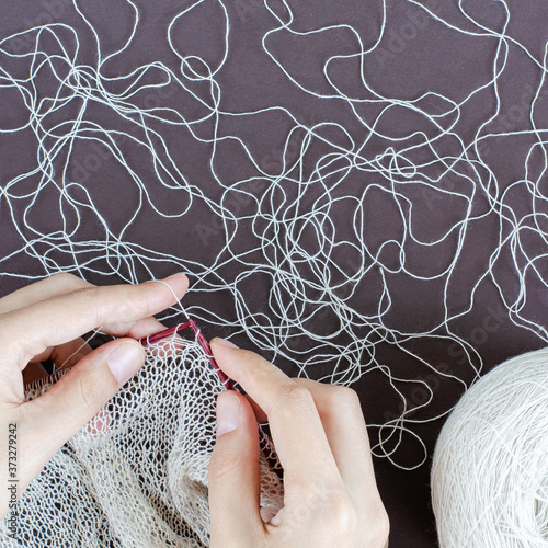 female hands knitting scarf with white lace yarn on wood knitting needles. dark background, top view