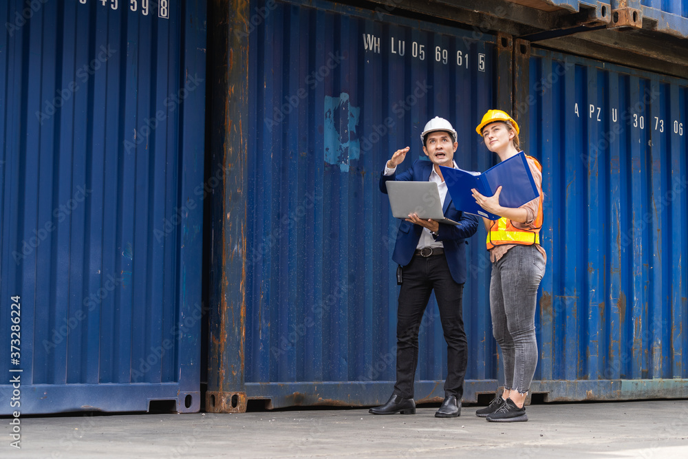 two engineer worker hold a laptop, document for checking a quality of containers box from cargo ship for export and import, blue container background two engineer worker hold a laptop, document for checking a quality of containers box from cargo ship for export and import, blue container background