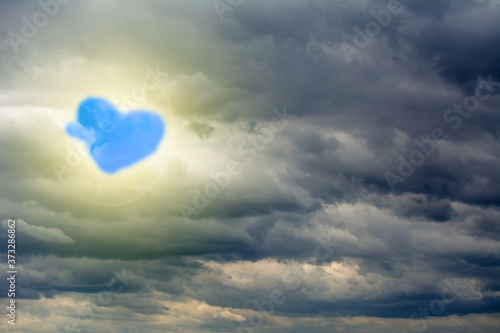 Glow through the clouds of the evening warm sun. Blue cloud in form of heart. Concept of love, peace and happiness.