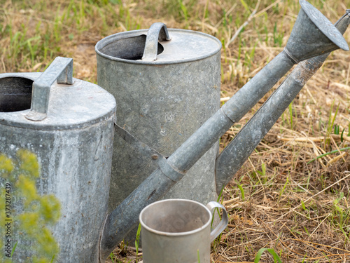 several old antique iron watering cans stand on the ground in the countryside