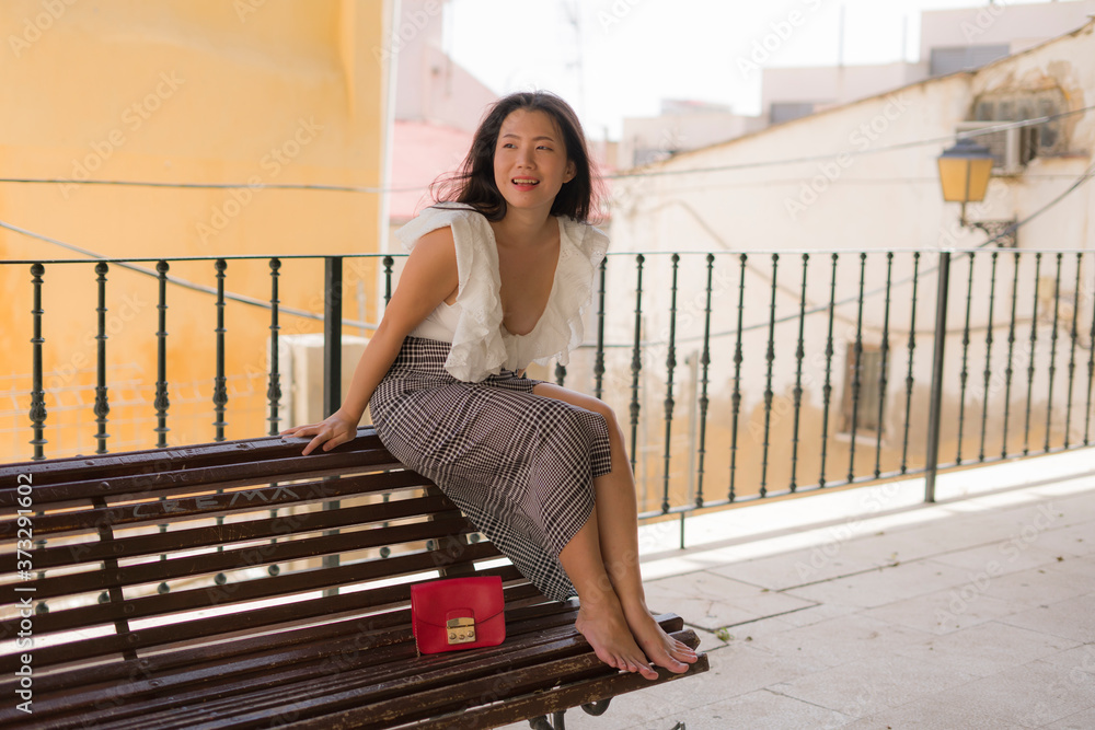 lifestyle portrait of young attractive and beautiful Asian Korean woman sitting outdoors at city park bench happy and relaxed touring Seville town in Spain during holidays travel in Europe lifestyle portrait of young attractive and beautiful Asian Korean woman sitting outdoors at city park bench happy and relaxed touring Seville town in Spain during holidays travel in Europe
