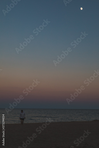 man standing at sea beach looking at moon