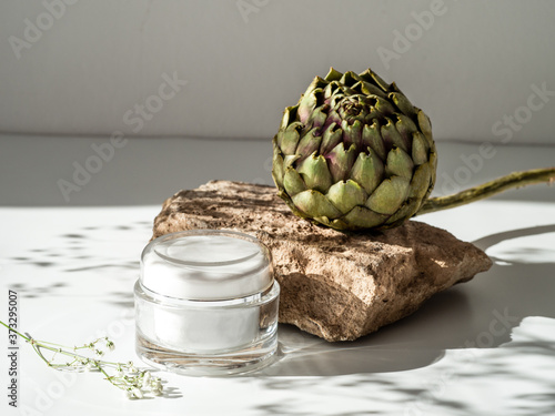 Cream mockup with geometric shape podium. Stone shape with artichoke flower and blank cream over white background. Copy space photo