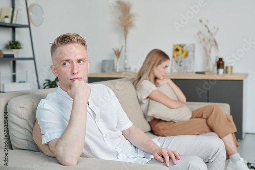 Young offended or annoyed man sitting on couch while ignoring his unhappy wife