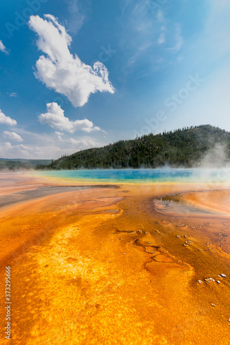 Orange and yellow bacterial mat at grand prismatic spring contrast with the blue hot spring vaporizing hot steam in the air - Yellowstone National Park, WY - USA