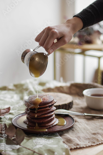 Fototapeta Naklejka Na Ścianę i Meble -  Chocolate pancakes with honey on a brown ceramic plate. Sweet breakfast on a table. Bright interior. Minimalism.