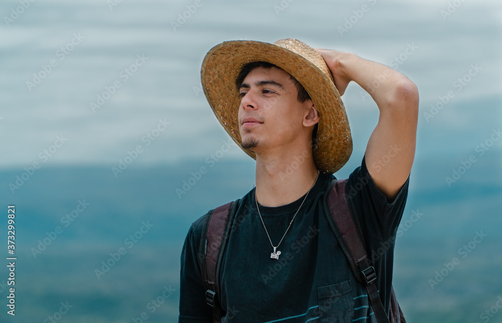 Hombre joven sostiene su sombrero mientras sonrie.
