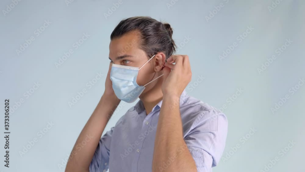 Handsome brunette man putting on hygienic mask. Static, bluish background Handsome brunette man putting on hygienic mask. Static, bluish background