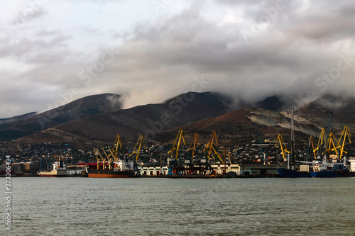 The seaport on the background of mountains during cloudy, cloudy weather in the mountains. Moored for unloading / loading sea ships against the background of mountains in the clouds. © Алекс Швачко