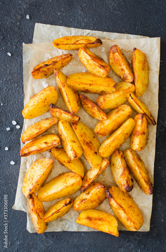 Golden spicy potato wedges fried or oven baked on dark table.