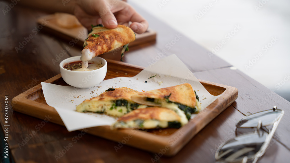 Vegetarian snack, piece of spinach and cheese Quesadilla holding by hand after dipped from the sauce in the warm tone color with copy space, food photography, mexican cuisine.