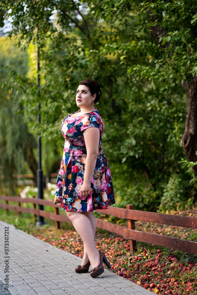 Naklejka premium Plus size fashion model in floral dress outdoors, beautiful fat woman with big breasts in nature