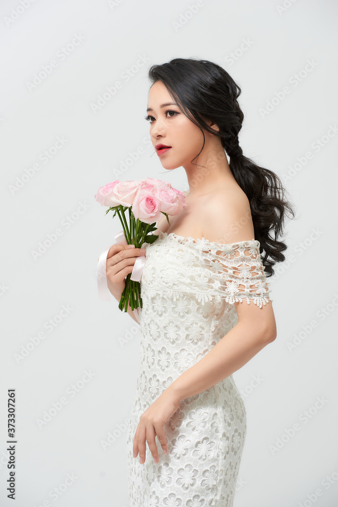 Naklejka premium Young beautiful woman in a white dress posing with a bouquet of roses