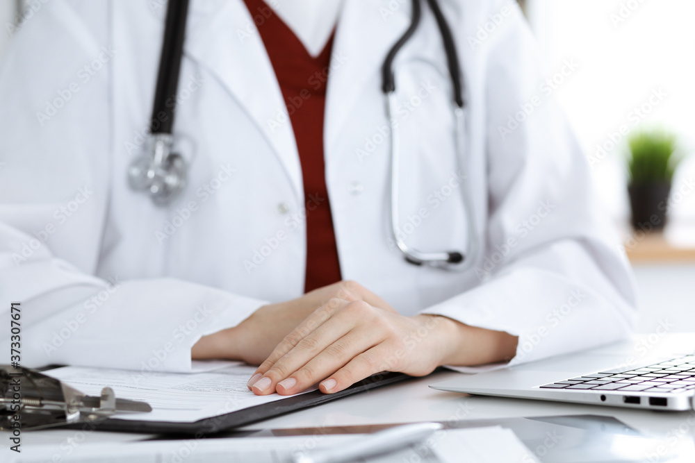 Unknown woman-doctor sitting at the table at working place, close-up of hands. Medicine concept Unknown woman-doctor sitting at the table at working place, close-up of hands. Medicine concept