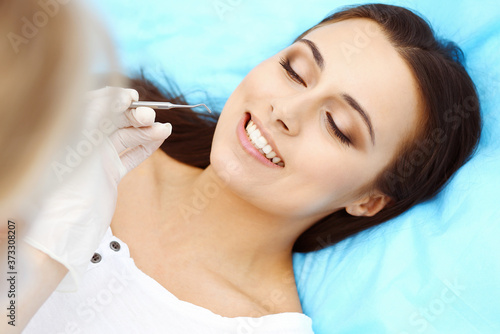 Young female patient visiting dentist office.Beautiful woman with healthy straight white teeth sitting at dental chair with open mouth during oral checkup while doctor working at teeth