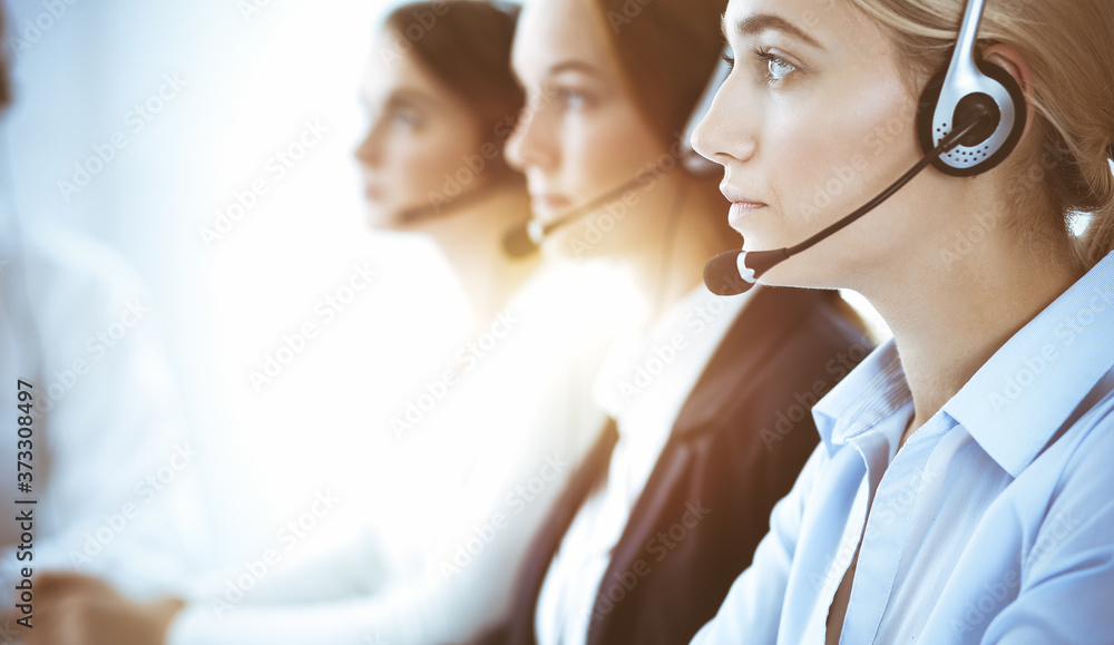 Call center and business people concept. Beautiful business woman with headphones consulting clients. Group of diverse phone operators at work in office Call center and business people concept. Beautiful business woman with headphones consulting clients. Group of diverse phone operators at work in office
