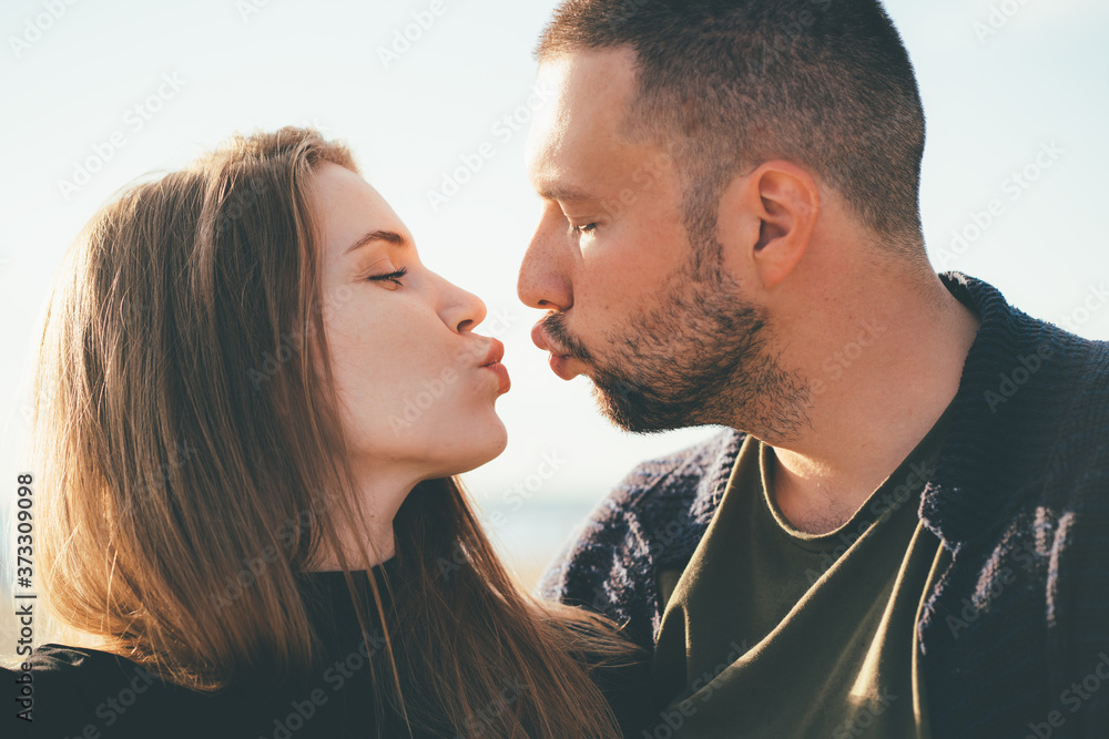 Man looking tenderly at woman and kissing. Young couple stands embracing. Family in love, sincere feelings of male and female. Waterfront. Close up portrait of beautiful people Man looking tenderly at woman and kissing. Young couple stands embracing. Family in love, sincere feelings of male and female. Waterfront. Close up portrait of beautiful people