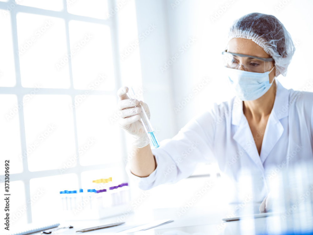 Professional female scientist in protective eyeglasses researching tube with reagents in laboratory. Concepts of medicine and science researching