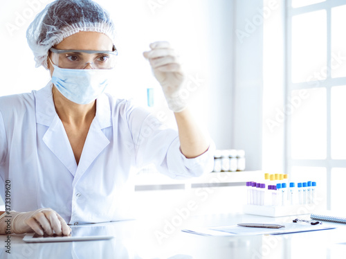 Professional female scientist in protective eyeglasses researching tube with reagents in laboratory. Concepts of medicine and science researching