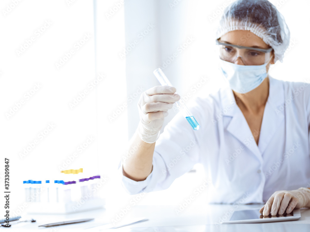 Professional female scientist in protective eyeglasses researching tube with reagents in laboratory. Concepts of medicine and science researching