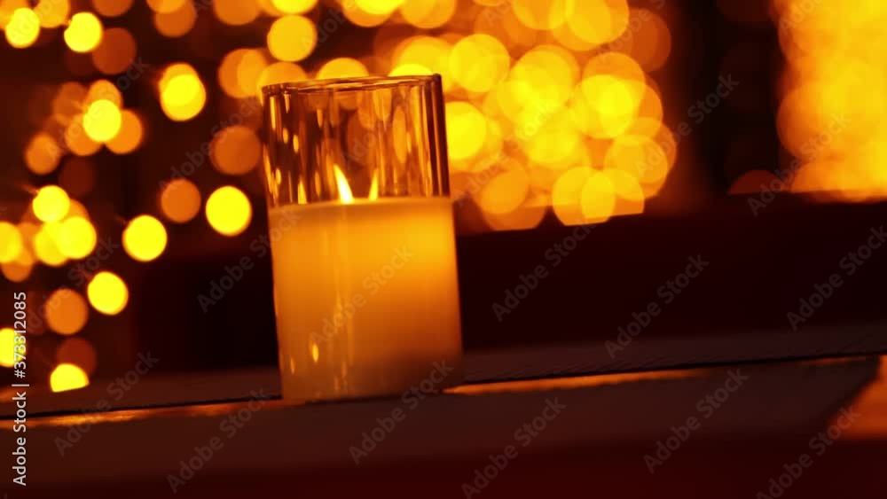 Burning candle in glass on the table in restaurant verandah - bright lights on a background Burning candle in glass on the table in restaurant verandah - bright lights on a background
