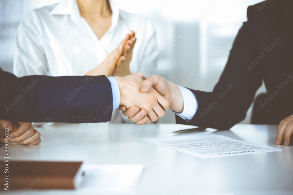Business people shaking hands at meeting or negotiation, close-up. Two unknown businessmen and a woman sitting at the desk in a modern office. Teamwork, partnership and handshake concept Business people shaking hands at meeting or negotiation, close-up. Two unknown businessmen and a woman sitting at the desk in a modern office. Teamwork, partnership and handshake concept