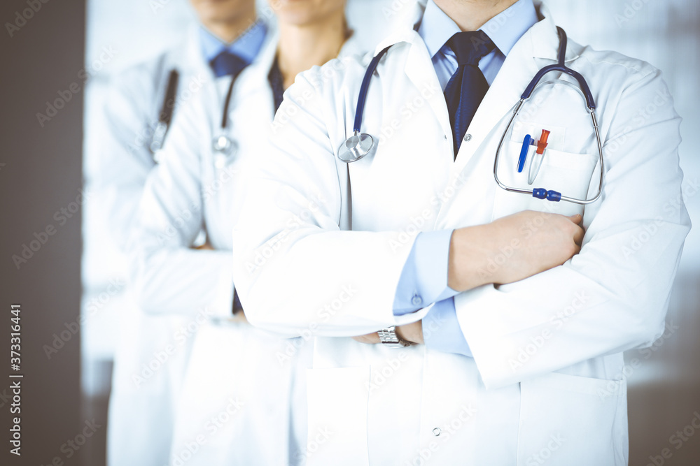 Group of modern doctors standing as a team with crossed arms and stethoscopes in hospital office. Physicians ready to examine and help patients. Medical help, insurance in health care, best desease Group of modern doctors standing as a team with crossed arms and stethoscopes in hospital office. Physicians ready to examine and help patients. Medical help, insurance in health care, best desease