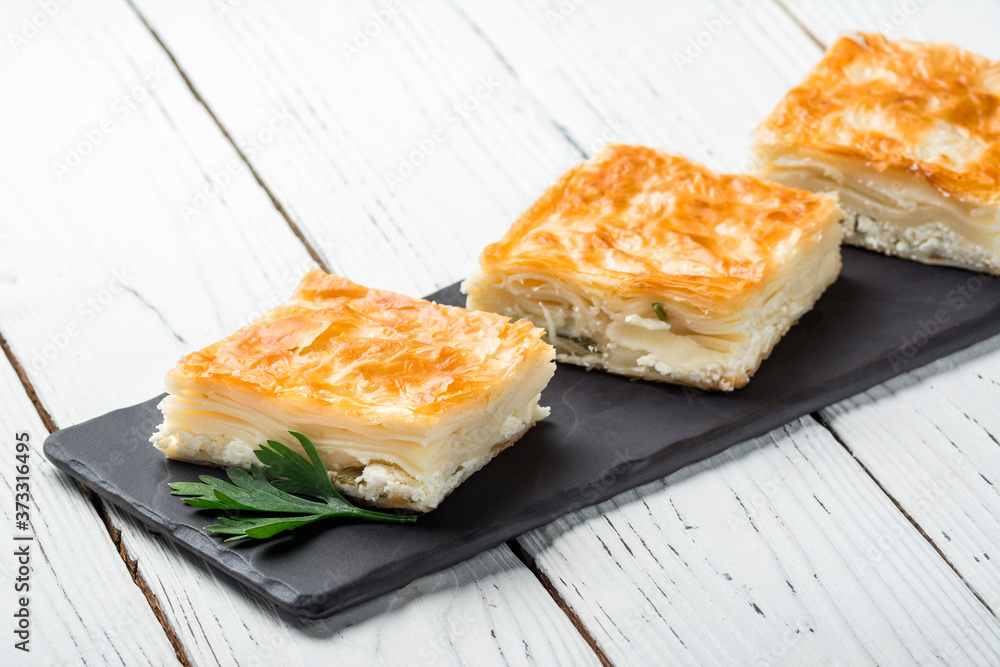 Turkish baklava, oriental sweets on a black dish for serving on a wooden white table. Horizontal format. Turkish baklava, oriental sweets on a black dish for serving on a wooden white table. Horizontal format.