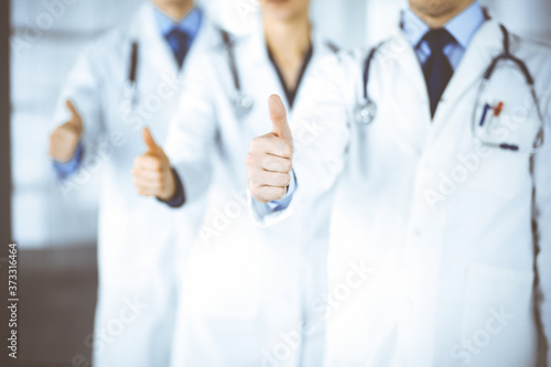 Group of unknown doctors stand as a team with thumbs up in a hospital office. Physicians ready to examine and help patients. Medical help, insurance in health care, best desease treatment and medicine