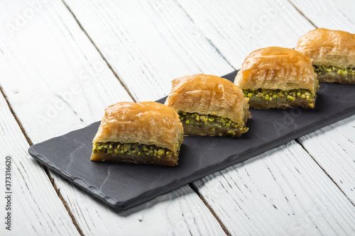 Turkish baklava, oriental sweets on a black dish for serving on a wooden white table. Horizontal format.