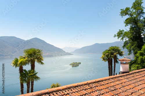 View over a Mediterranean roof with a fireplace between palm trees to Lake Maggiore and the Isola di Brissago in Switzerland