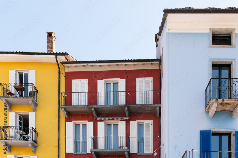 Colorful house front in the old town of Ascona in Switzerland in yellow, red and blue with a bright blue sky.