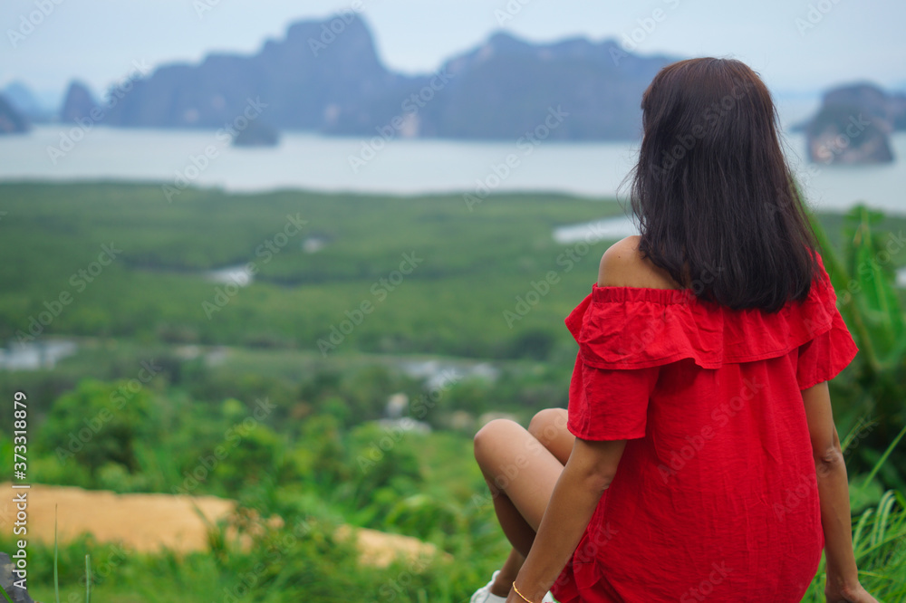 Back view of a traveling woman in a red dress looking at an amazing view with cliffs and a tropical beach. Pointing to the mountain. The concept of freedom and adventure.