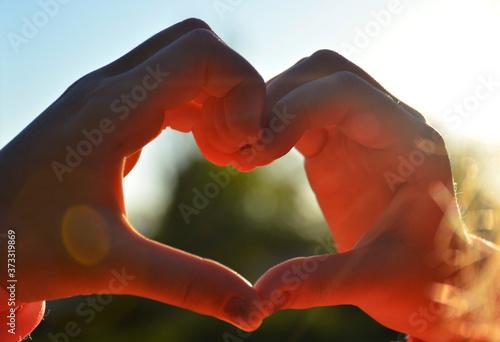heart from female hands at sunset. the sun illuminates the hands in orange