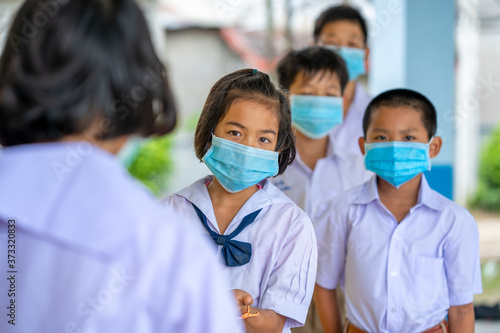 Asia elementary children spraying classmate's hands with disinfectant while wearing protective face masks on a class in the classroom.