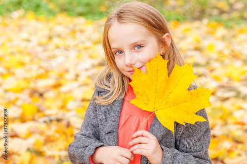 Happy young girl playing with falling yellow leaves in beautiful autumn park on nature walks outdoors. Little child holding autumn orange maple leaf