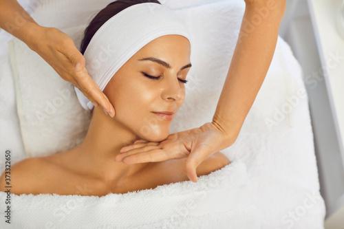 Hands of cosmetologist making facial beauty massage for relaxed lying young woman