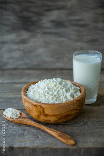 Fresh cottage cheese in a wooden bowl with a spoon with a glass of milk on a wooden old background photo