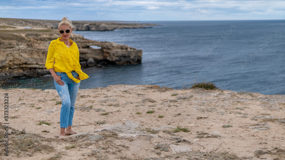Happy lady in a yellow shirt young with a kind look blue clouds during the day and in the summer on a rocky beach