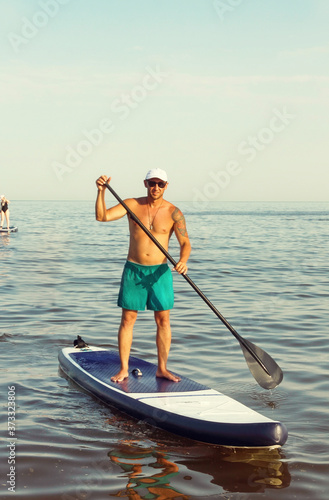 men is training on a SUP board in the summer sea.