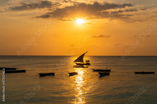 Warm golden sunset over the sea (Indian Ocean), with dark boats shapes and traditional Dhow coming back for night from fishing, Zanzibar, Tanzania. © Cleop6atra