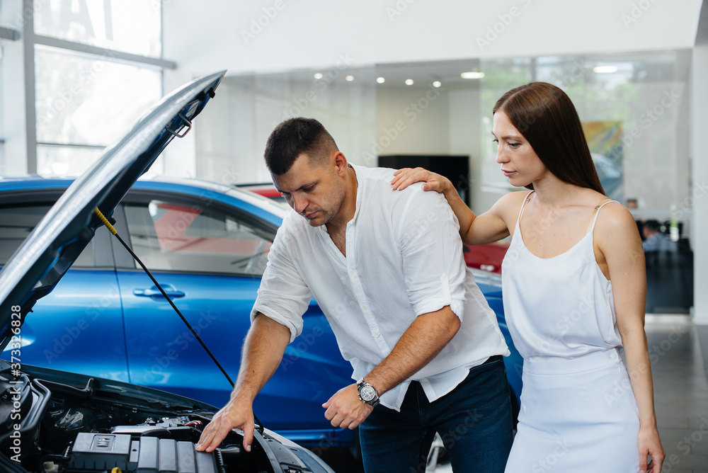 A young couple chooses a new car at the dealership and consults with a representative of the dealership. Used cars for sale. Dream fulfillment