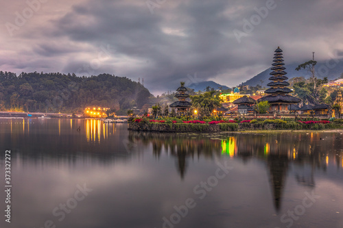 Mountains and blue rain clouds over Pura Ulun Danu Bratan Temple in the evening with lights on