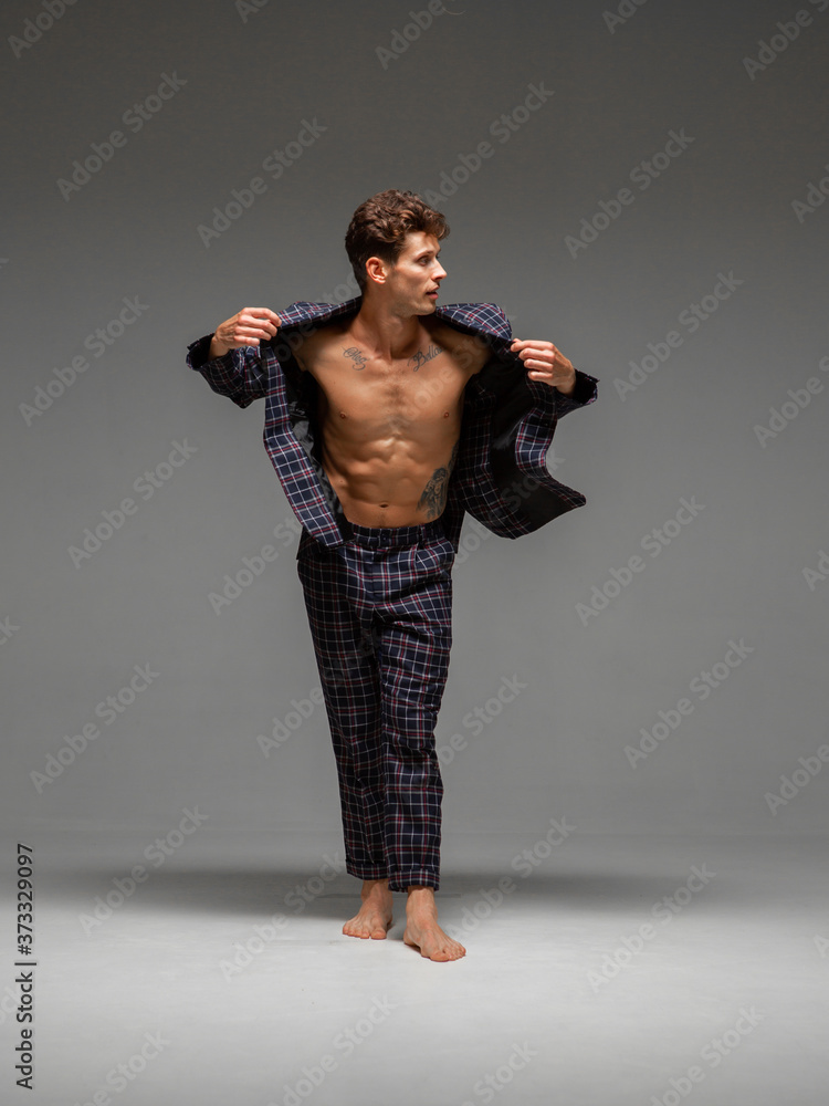 Stylish young guy in suit with a wide-open jacket and naked torso stand in studio on gray background Stylish young guy in suit with a wide-open jacket and naked torso stand in studio on gray background
