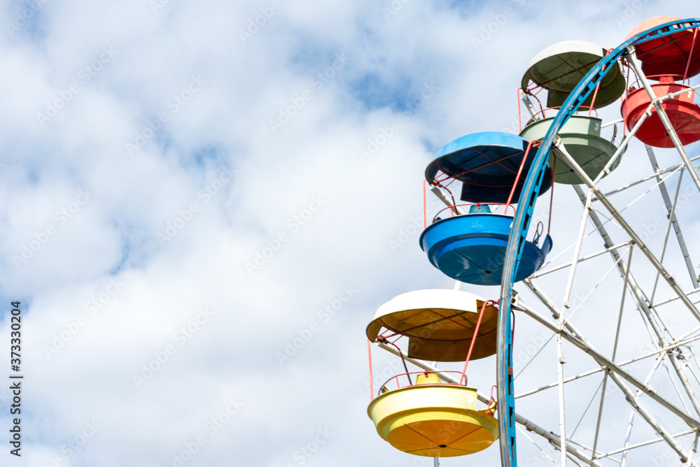 Colorful cabs of ferris wheels on the cloudy sky background in amusement park