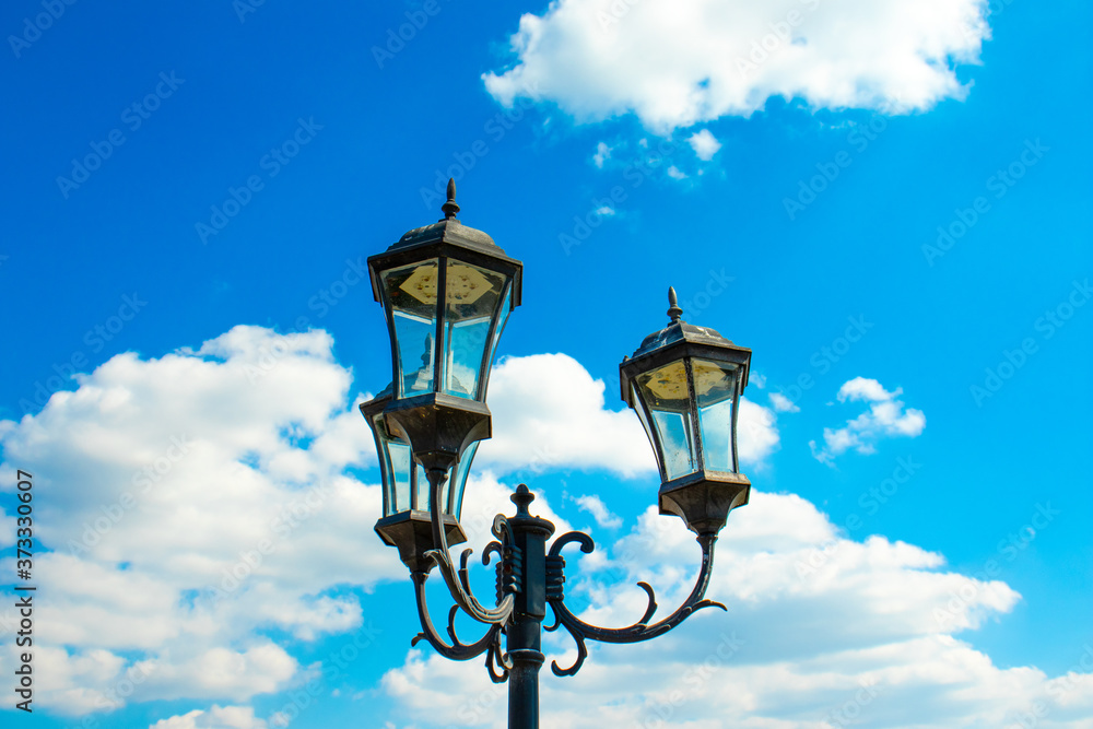 Beautiful garden lantern against a background of blue sky and white clouds. Bottom view. Sunny summer day.