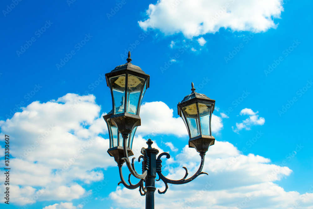 Beautiful garden lantern against a background of blue sky and white clouds. Bottom view. Sunny summer day. Beautiful garden lantern against a background of blue sky and white clouds. Bottom view. Sunny summer day.
