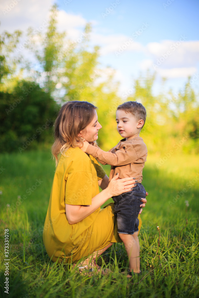Cute baby boy and mother hug each other on green lawn. Summertime photography for ad or blog about motherhood Cute baby boy and mother hug each other on green lawn. Summertime photography for ad or blog about motherhood