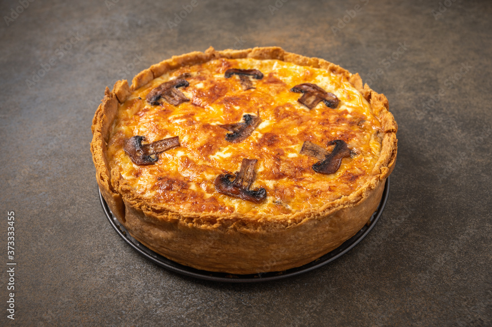 Traditional French pie quiche with mushrooms and cheese on a dark textured background, close up, copy space