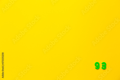 A green plastic toy number ninety-three is located in the lower right corner on a yellow background © Hanna